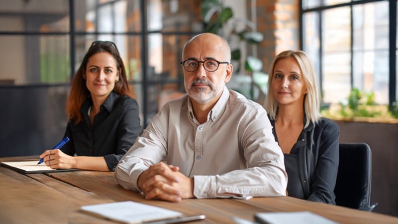 man-with-glasses-balding-man-black-shirt-sits-table-with-other-people